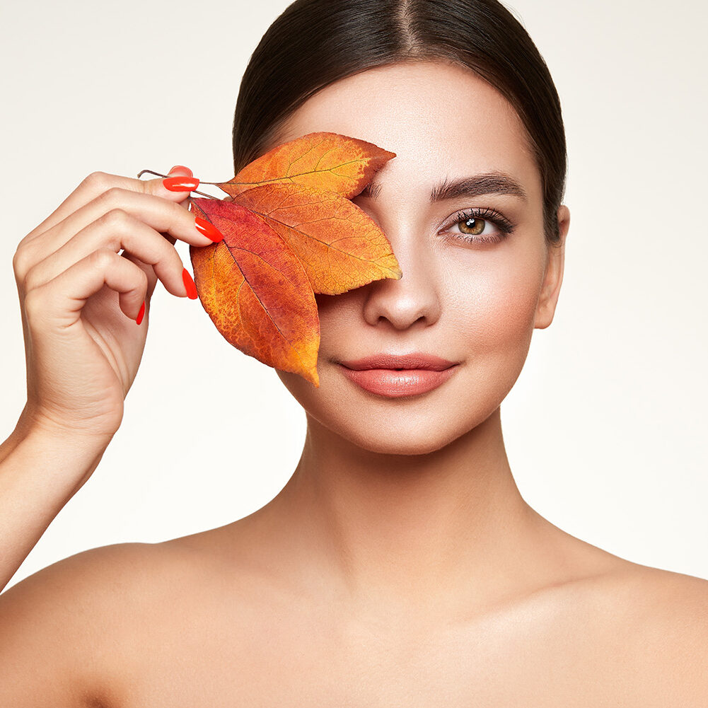 Portrait of beautiful young woman with autumn leafs. Healthy clean fresh skin natural make up beauty eyes and red nails